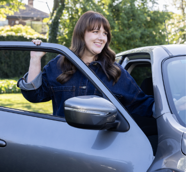Smiling woman sitting in the driver's seat of her car, wearing a seatbelt