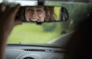Woman smiling in the rear view mirror of a car