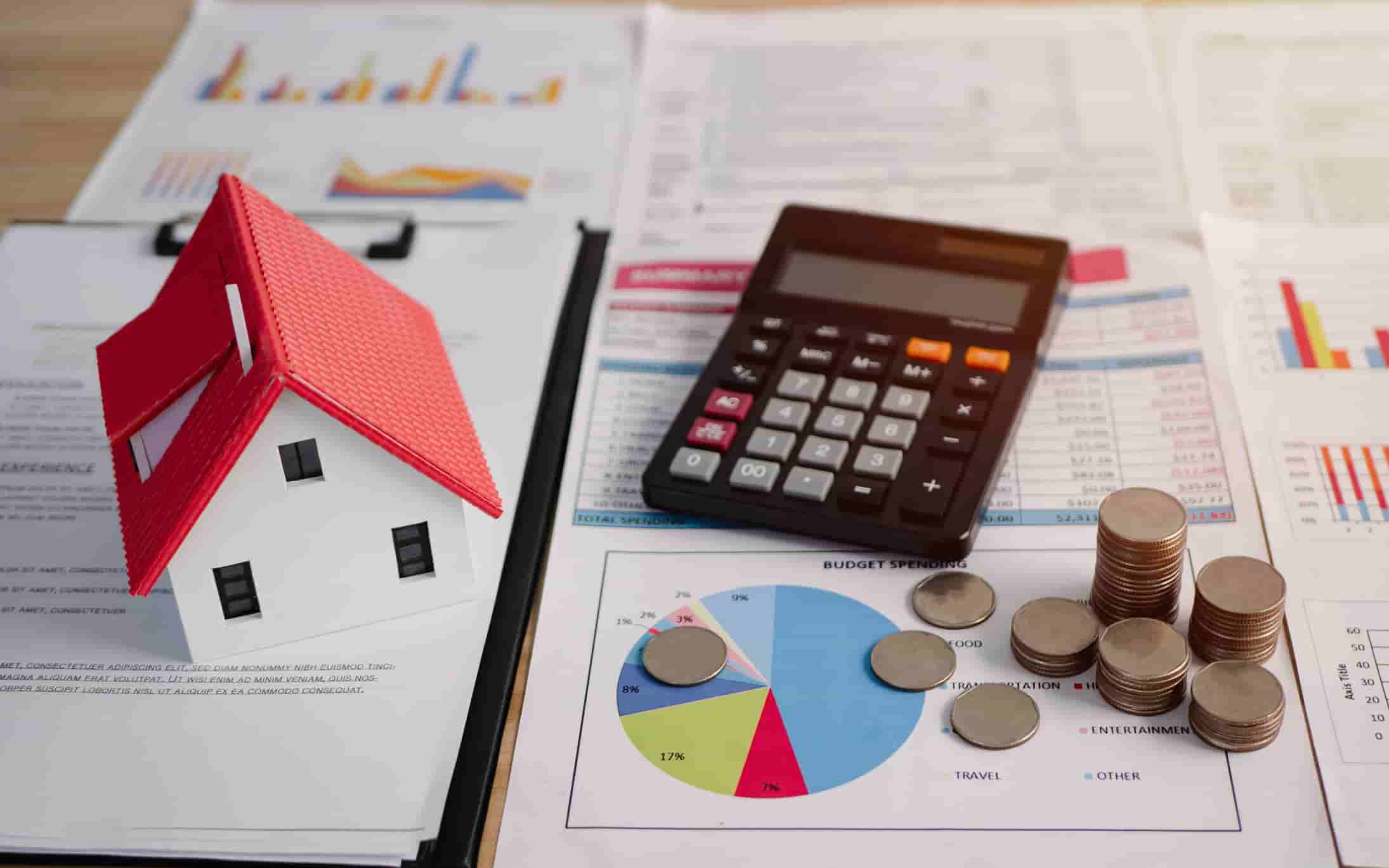 Model house beside a calculator, coins and financial charts, illustrating how to work out mortgage borrowing and costs
