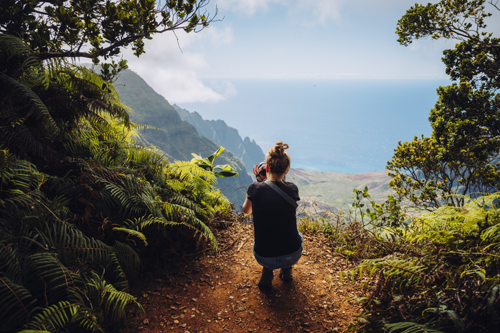 Woman standing on top of a mountain looking out at the sea with a camera in her hands
